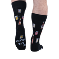 Back view of someone wearing black beer pattern socks, showing the sole of the left foot with white text reading ALE YEAH!