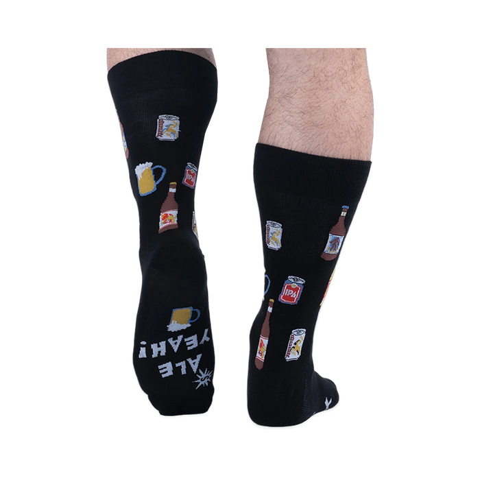 Back view of someone wearing black beer pattern socks, showing the sole of the left foot with white text reading ALE YEAH!