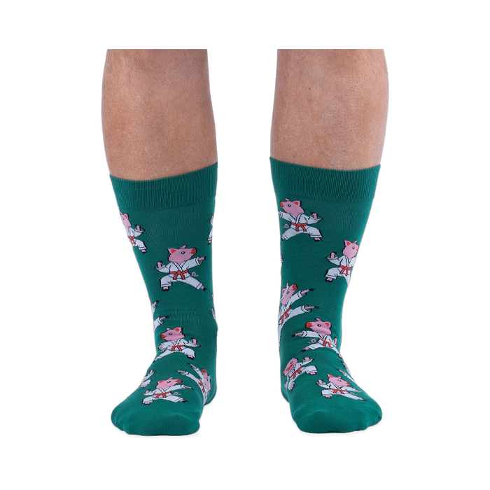 Front view of a person's lower legs wearing green socks with a pattern of pink pigs in white karate uniforms.