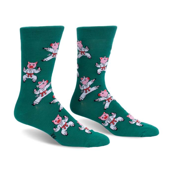 Pair of green crew socks featuring a pattern of pink pigs wearing white karate uniforms and red belts in martial arts poses.