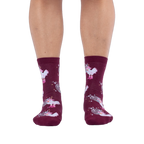 Front view of someone wearing burgundy crew socks with a disco ball and cowboy chicken pattern against a black background.