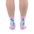 Back view of legs wearing light blue socks showing brown dachshunds wearing pink sunglasses sitting next to cocktails.