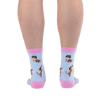 Back view of legs wearing light blue socks showing brown dachshunds wearing pink sunglasses sitting next to cocktails.