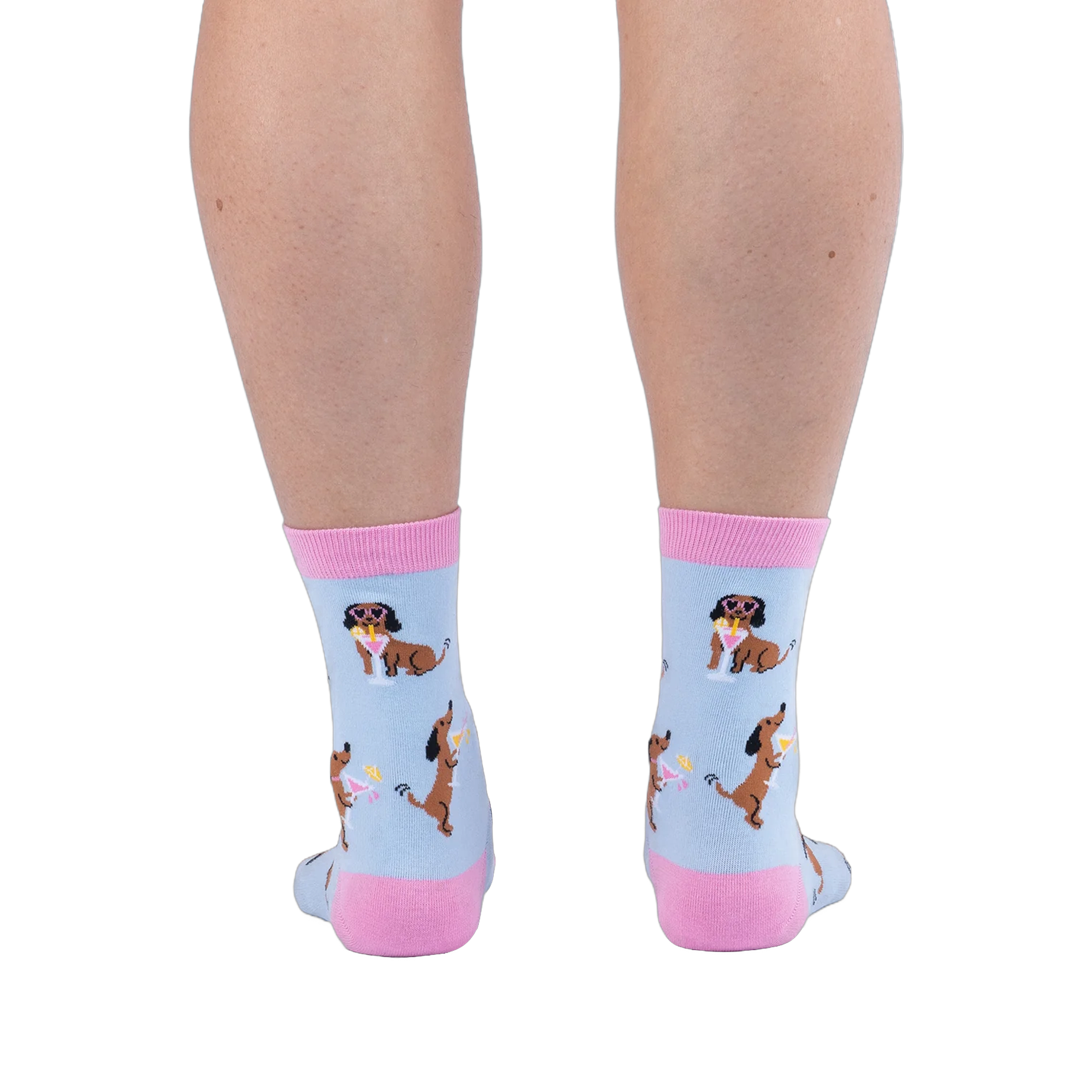 Back view of legs wearing light blue socks showing brown dachshunds wearing pink sunglasses sitting next to cocktails.