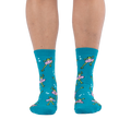 Front view of someone wearing teal crew socks featuring a pattern of green frogs in pink tutus on a black background.