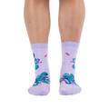 Front view of a person wearing light purple socks showing a pattern of teal octopuses wearing tiny pink socks.