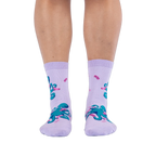 Front view of a person wearing light purple socks showing a pattern of teal octopuses wearing tiny pink socks.