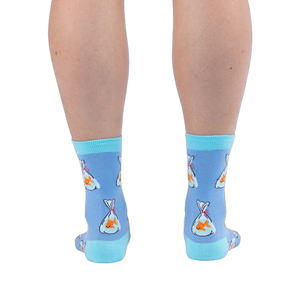 Back view of legs wearing light blue crew socks showing orange goldfish in plastic bags tied with red string and aqua heels.
