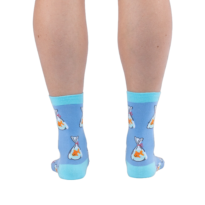Back view of legs wearing light blue crew socks showing orange goldfish in plastic bags tied with red string and aqua heels.