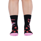 Front view of legs wearing black socks showing the pink book graphic, wrap-around text, lit matches, and flaming hearts.