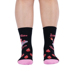 Front view of legs wearing black socks showing the pink book graphic, wrap-around text, lit matches, and flaming hearts.