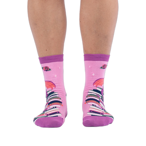 Front view of pink socks worn on legs, showing a tall stack of colorful books going up the shin with red roses at the top.
