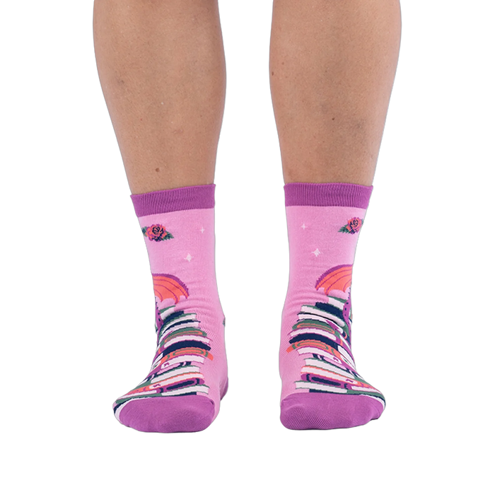 Front view of pink socks worn on legs, showing a tall stack of colorful books going up the shin with red roses at the top.