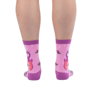 Back view of pink socks on legs, showing the back of a purple dragon with orange wings and scattered roses on the calves.
