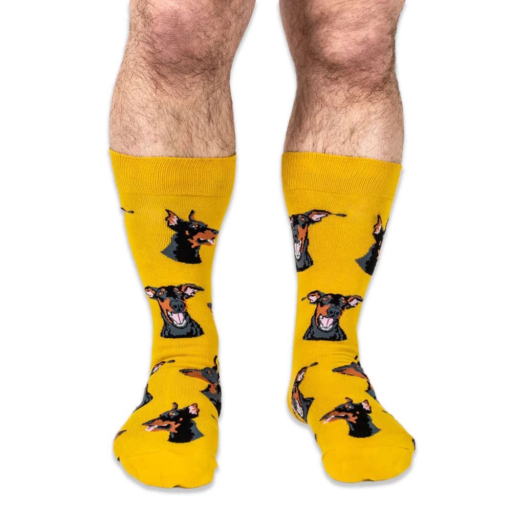 Front view of a person wearing yellow crew socks patterned with Doberman dog heads with big smiles and pink tongues.
