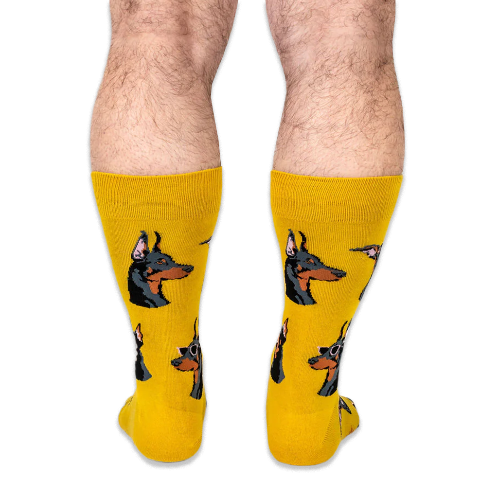 Back view of a person wearing bright yellow socks showing the profile of Doberman heads with classic black and tan markings.