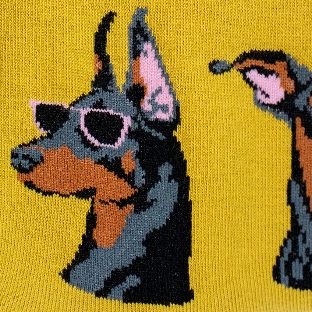 Close-up knit texture of a yellow sock showing a black and tan Doberman wearing pink-rimmed sunglasses.