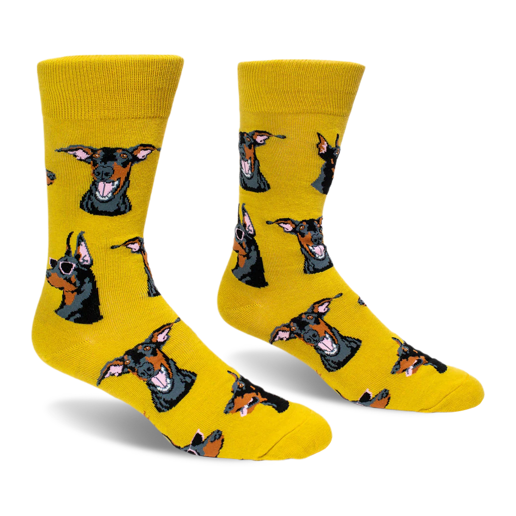 A pair of bright yellow crew socks featuring a pattern of black and tan Doberman dog heads, some wearing pink sunglasses.