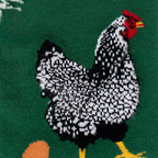 Close-up knit detail of a black and white speckled chicken with a red comb and yellow feet next to an orange egg.