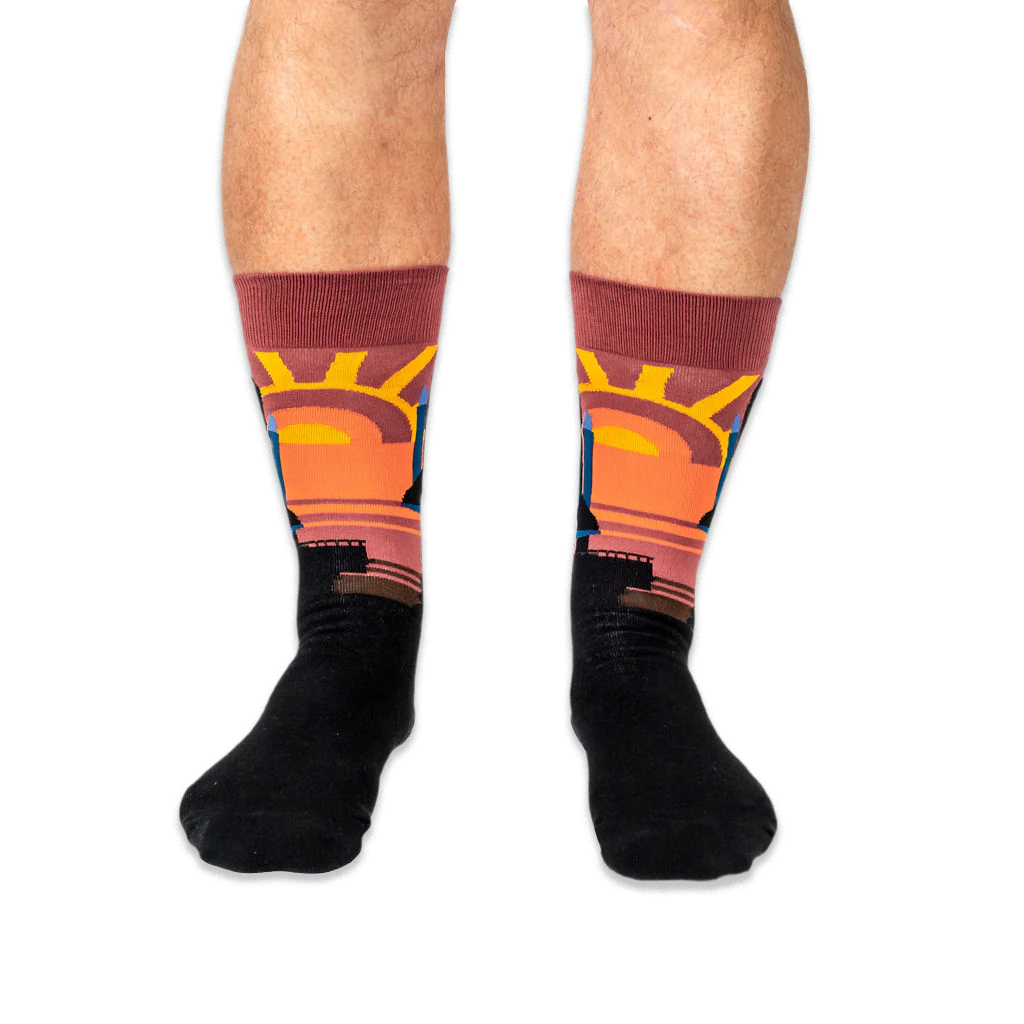 Front view of legs wearing black crew socks with a prominent warm-toned sunset design on the shins.