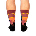 Back view of legs wearing space shuttle socks, showing the colorful striped sunset pattern wrapping around the calves.