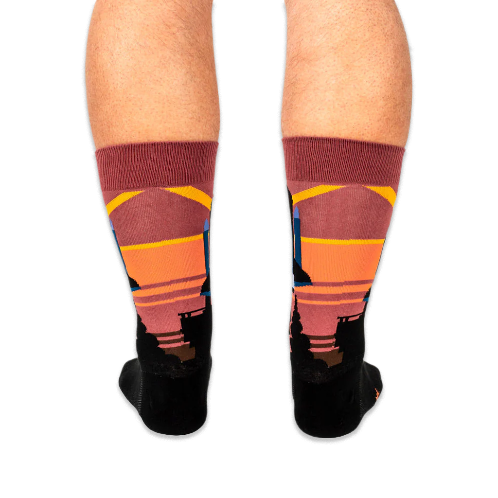Back view of legs wearing space shuttle socks, showing the colorful striped sunset pattern wrapping around the calves.