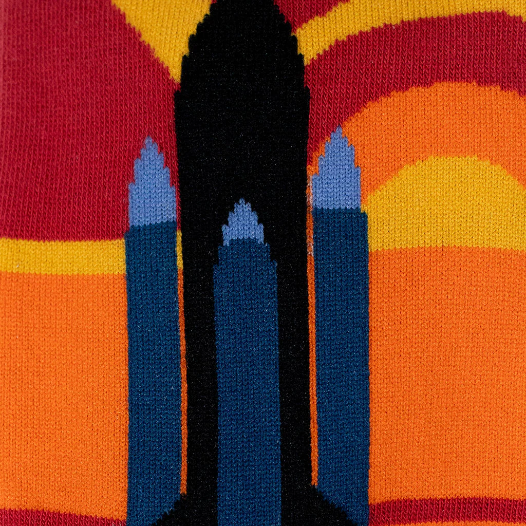 Macro shot of knitted sock fabric detailing the blue and black space shuttle silhouette against a warm striped background.