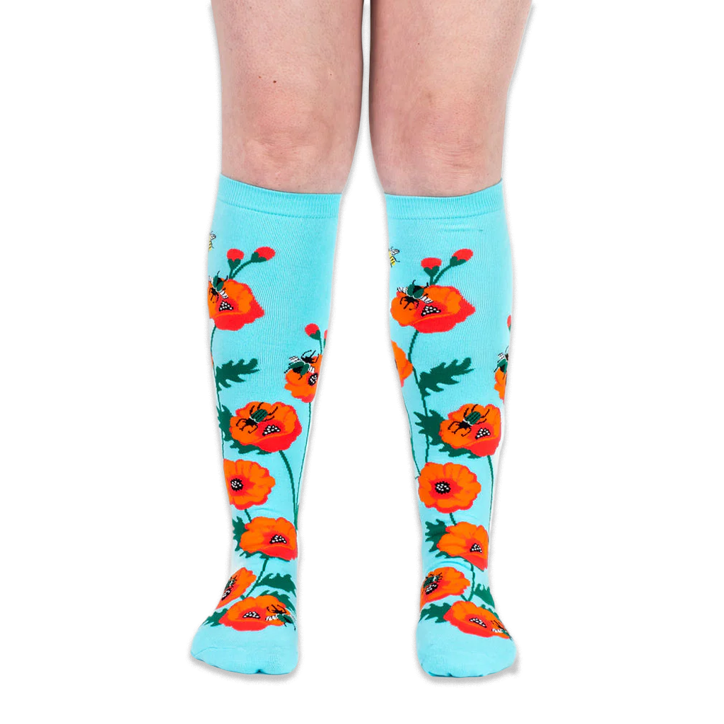 Front view of legs wearing bright turquoise knee-high socks patterned with bold red poppies and flying bumblebees.