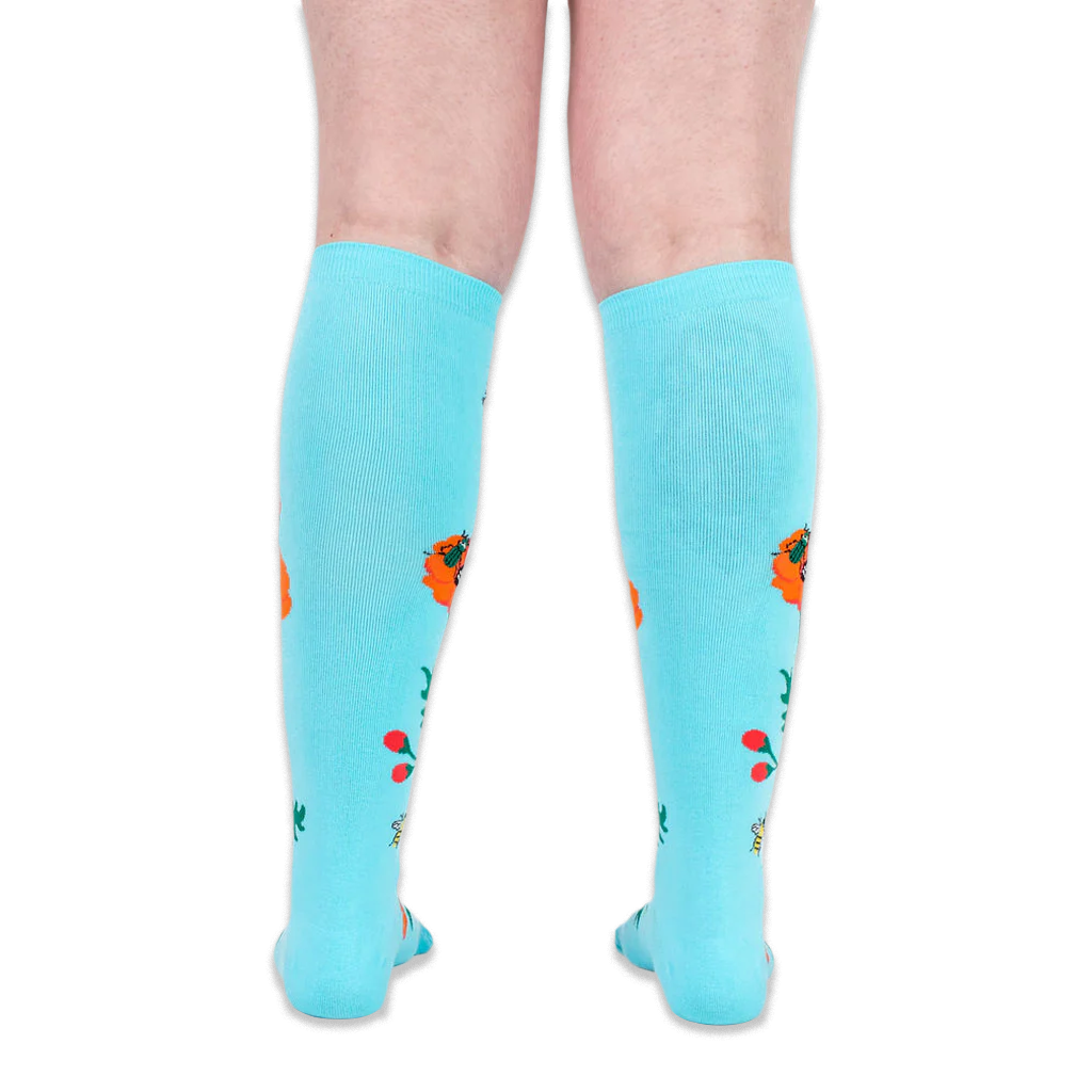 Back view of legs wearing turquoise knee-high socks, showing solid blue fabric with floral designs along the sides.