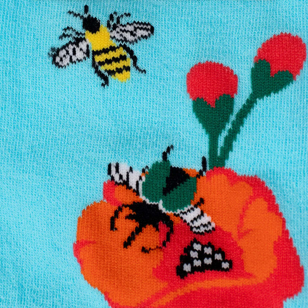 Close-up of blue knit sock fabric showing a yellow bumblebee, a green bug, red poppy petals, and two flower buds.