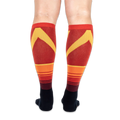 Back view of the knee-high socks being worn, displaying a bold yellow chevron pattern over horizontal orange stripes.