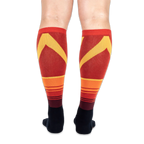 Back view of the knee-high socks being worn, displaying a bold yellow chevron pattern over horizontal orange stripes.