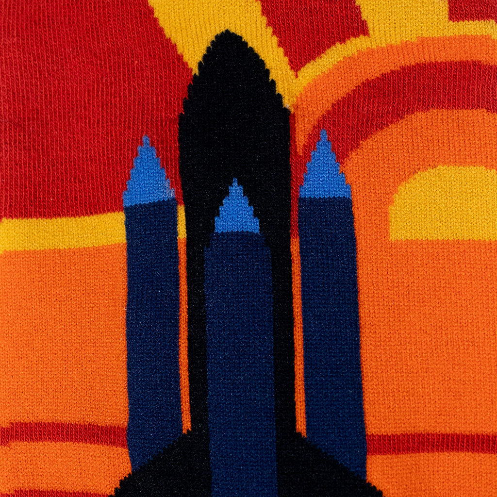 Close-up of the knit sock fabric showing a black and blue space shuttle design over a bright yellow and orange background.