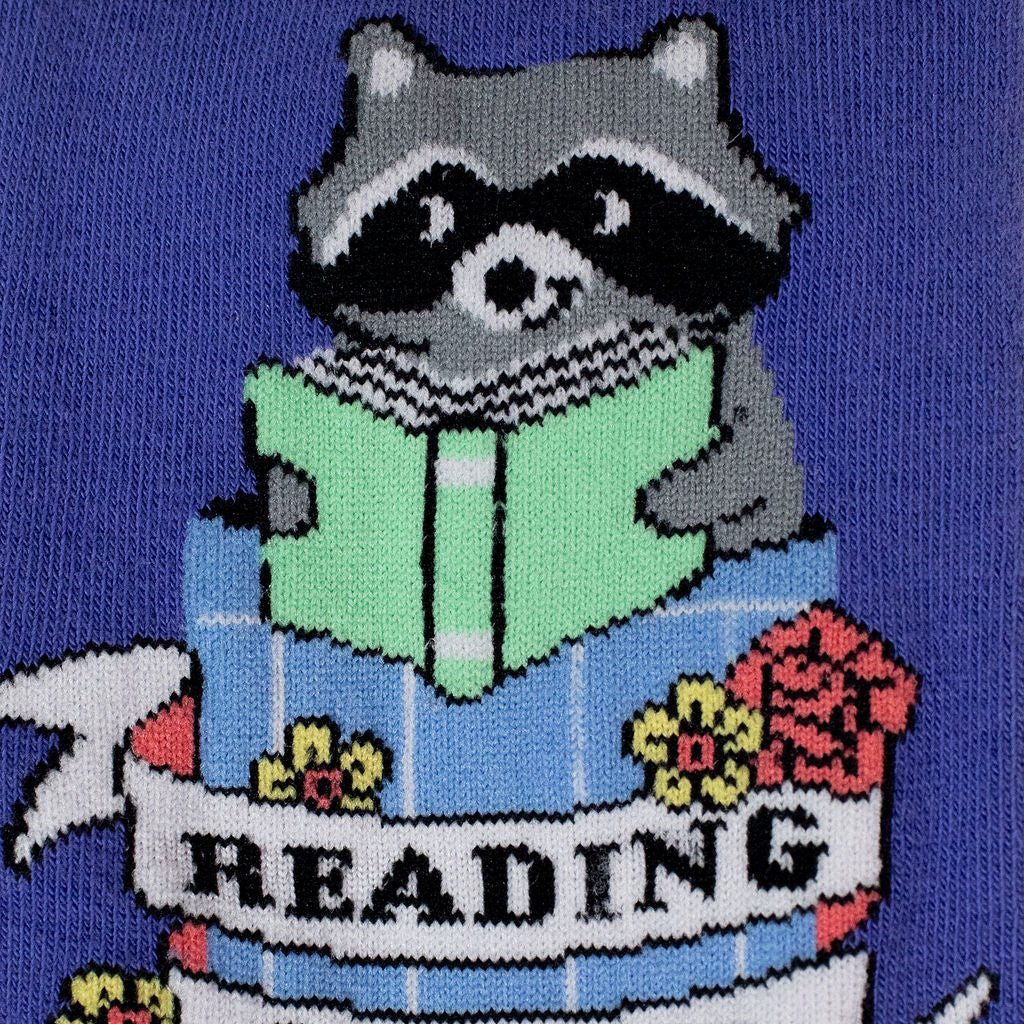 Close-up of the knit design showing a raccoon holding a green book inside a blue trash can with flowers and a Reading banner.