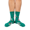 Someone wearing green crew socks with reading frogs and red mushrooms, viewed from the front against a black background.