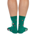 View from the back of someone wearing green crew socks featuring a pattern of red flowers and green frogs on mushrooms.