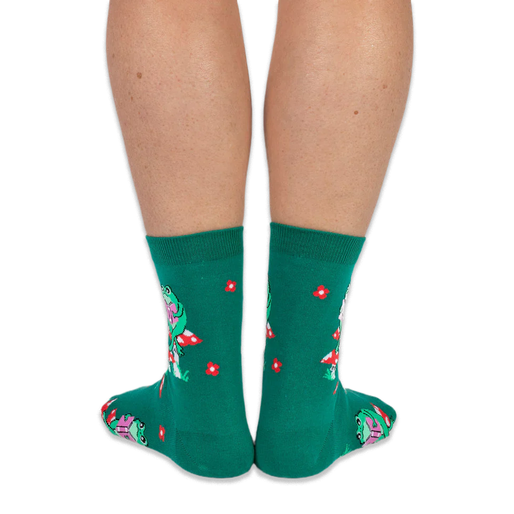View from the back of someone wearing green crew socks featuring a pattern of red flowers and green frogs on mushrooms.