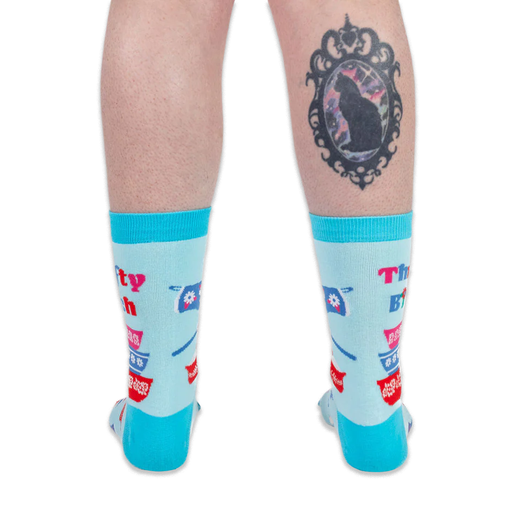 Back view of a person wearing light blue retro kitchen socks. The person has a black cat cameo tattoo on their calf.