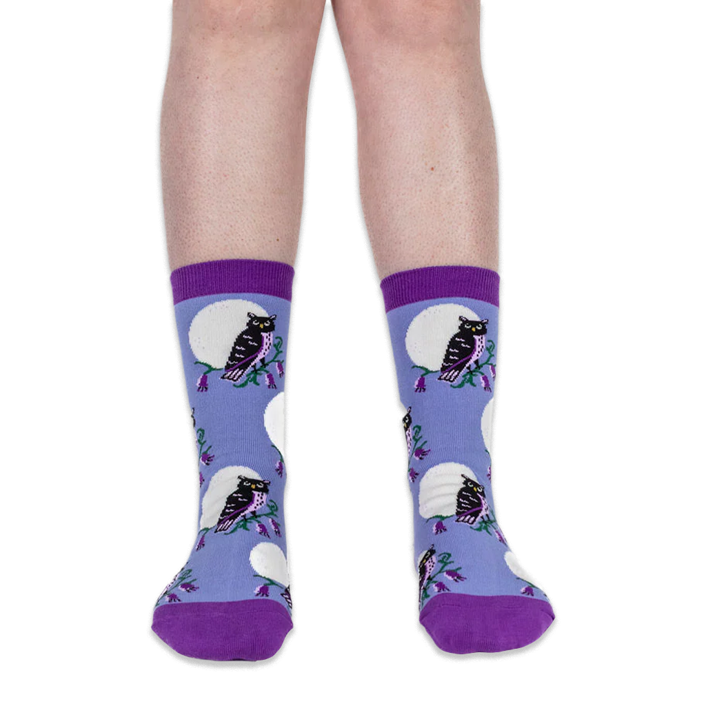 Front view of legs wearing light blue crew socks with black owls and white full moons against a solid black background.