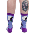 Back view of legs wearing blue owl socks. The right calf features a black cat cameo tattoo on a solid black background.