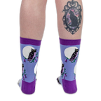 Back view of legs wearing blue owl socks. The right calf features a black cat cameo tattoo on a solid black background.