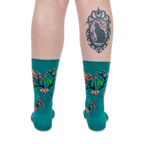 Back view of legs wearing teal bird socks. The person has a large framed black cat tattoo on their right calf.
