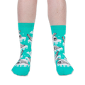 Front view of someone wearing bright teal crew socks with grey seal pups on icebergs against a black background.