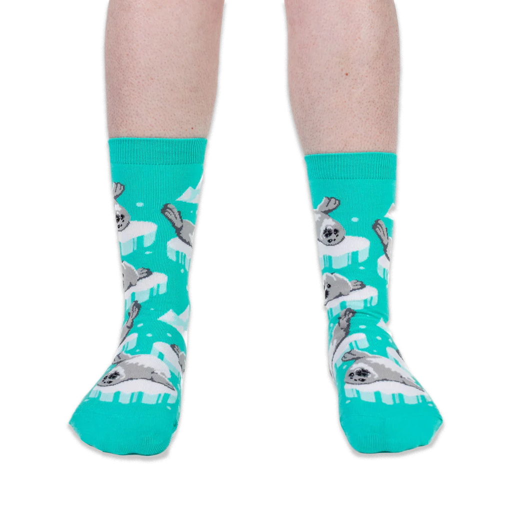 Front view of someone wearing bright teal crew socks with grey seal pups on icebergs against a black background.