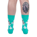Back view of someone wearing teal seal socks on a black background, showing a black cat cameo tattoo on their right calf.