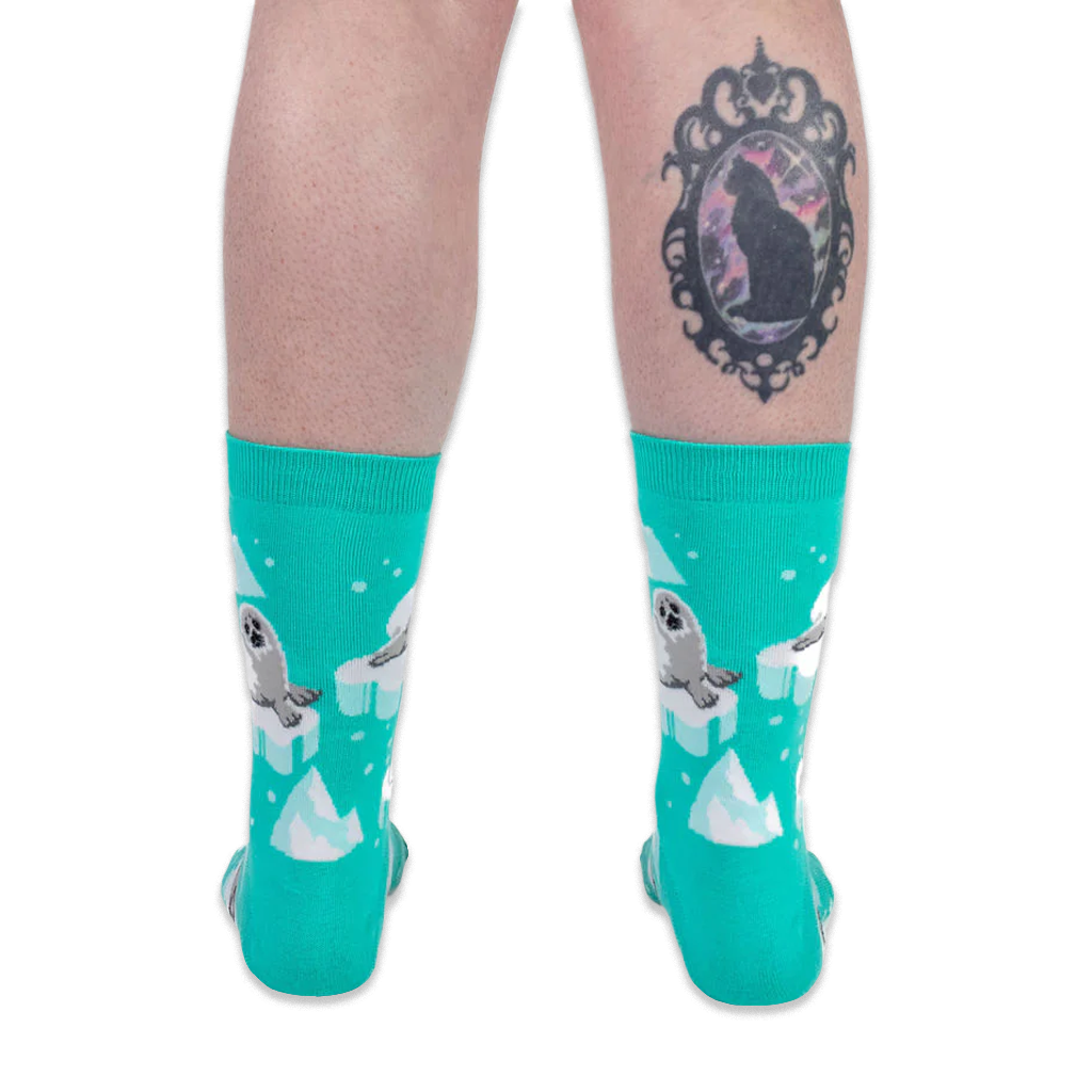 Back view of someone wearing teal seal socks on a black background, showing a black cat cameo tattoo on their right calf.