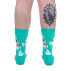 Back view of someone wearing teal seal socks on a black background, showing a black cat cameo tattoo on their right calf.