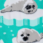 Close-up knit detail of the teal sock showing two fluffy grey and white seal faces resting on white ice.