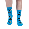 Front view of someone wearing bright blue crew socks with an orca and musical instrument pattern against a black background.