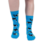 Front view of someone wearing bright blue crew socks with an orca and musical instrument pattern against a black background.
